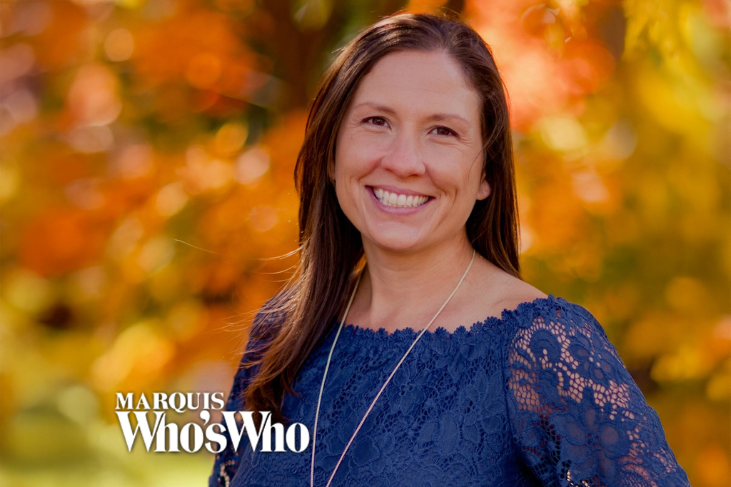 Smiling woman with long brown hair in a blue lace top outdoors during autumn, Marquis Who's Who logo in the lower-left corner.