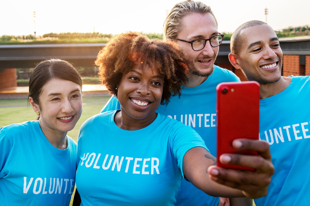 Four volunteers in matching blue shirts take a group selfie outdoors.